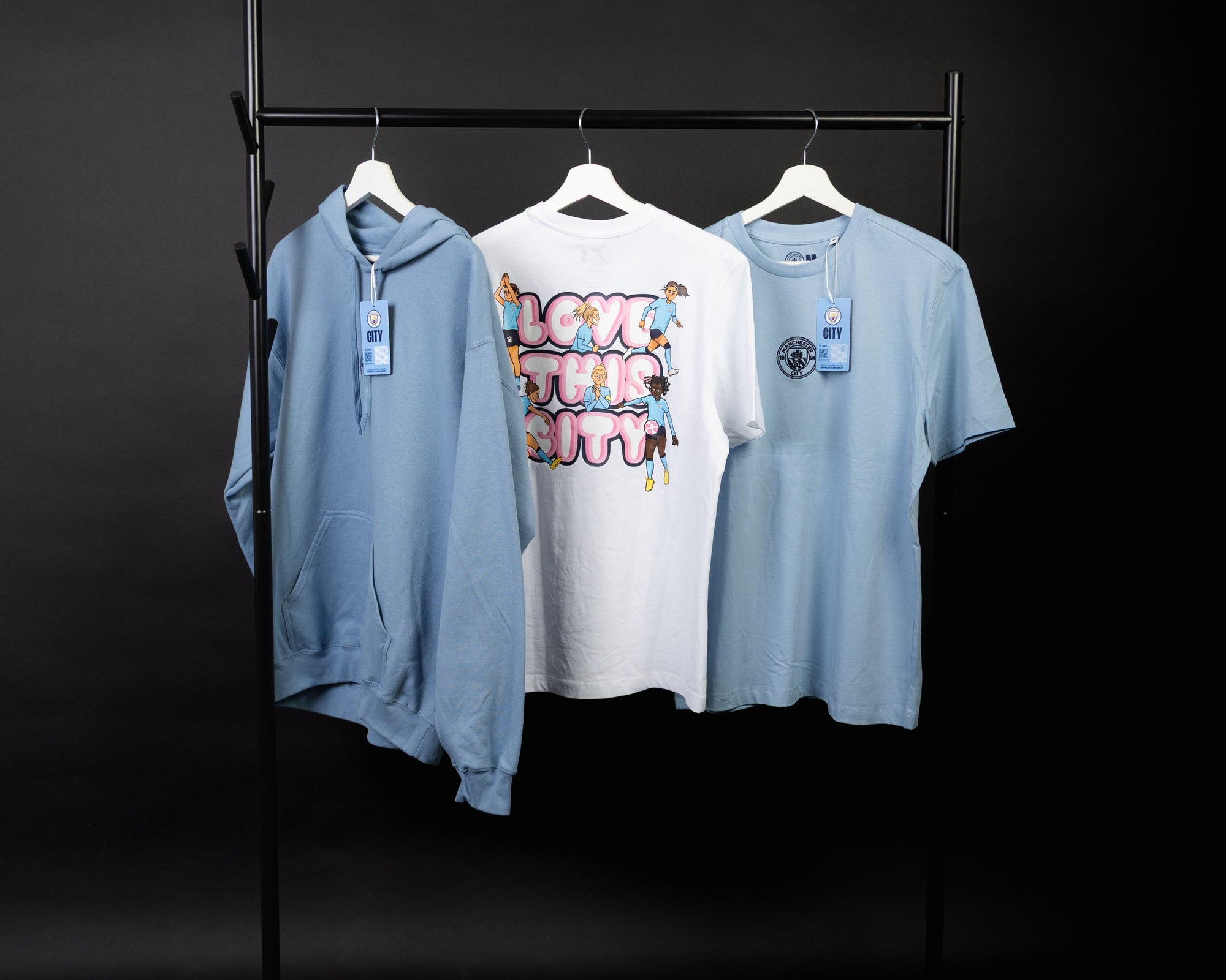 Women’s football hoodies and t-shirts from the AFTA Studios Manchester City collection displayed on a rail.